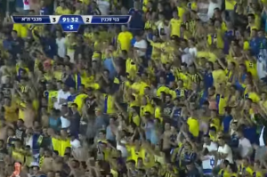 Maccabi TA fans cheering near end of soccer match.