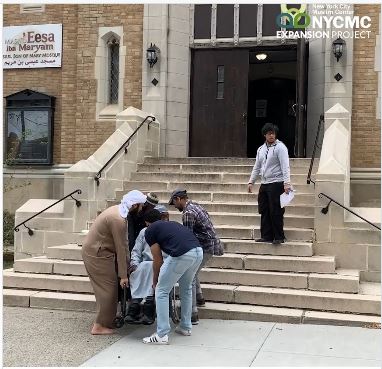 carrying a wheelchair-bound person up the stairs to the NYC mosque entrance